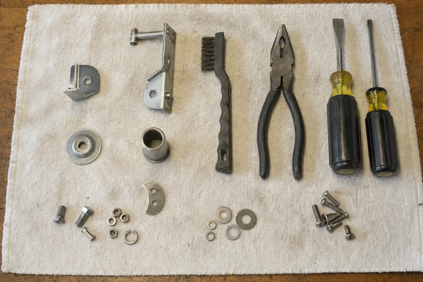 Hinge brackets, a flanged bearing, a bushing, bolts and hand tools laid out in rows on a workbench towel